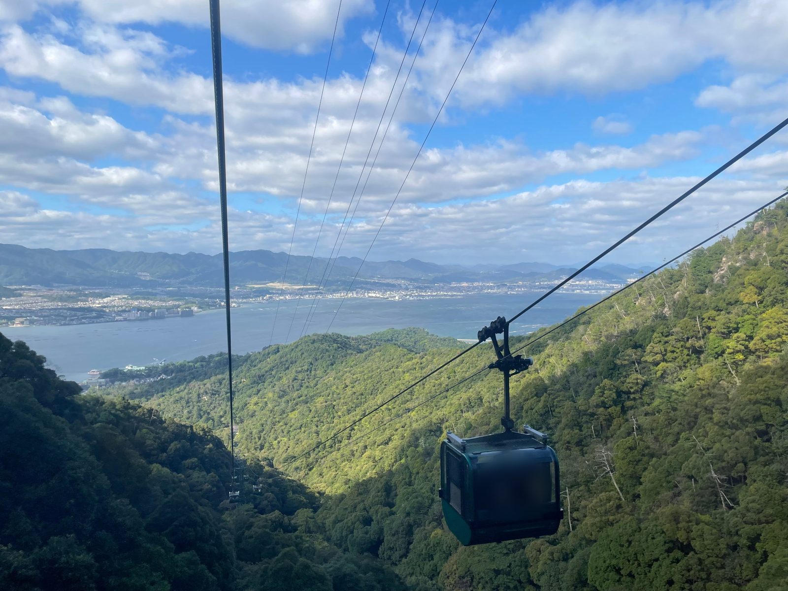 Miyajima Ropeway gondola above green forest with the sea and Hiroshima in the distance